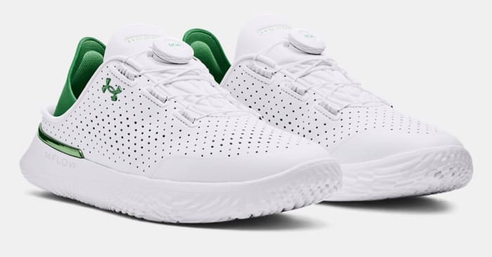 Side view of white and green Under Armour shoes.